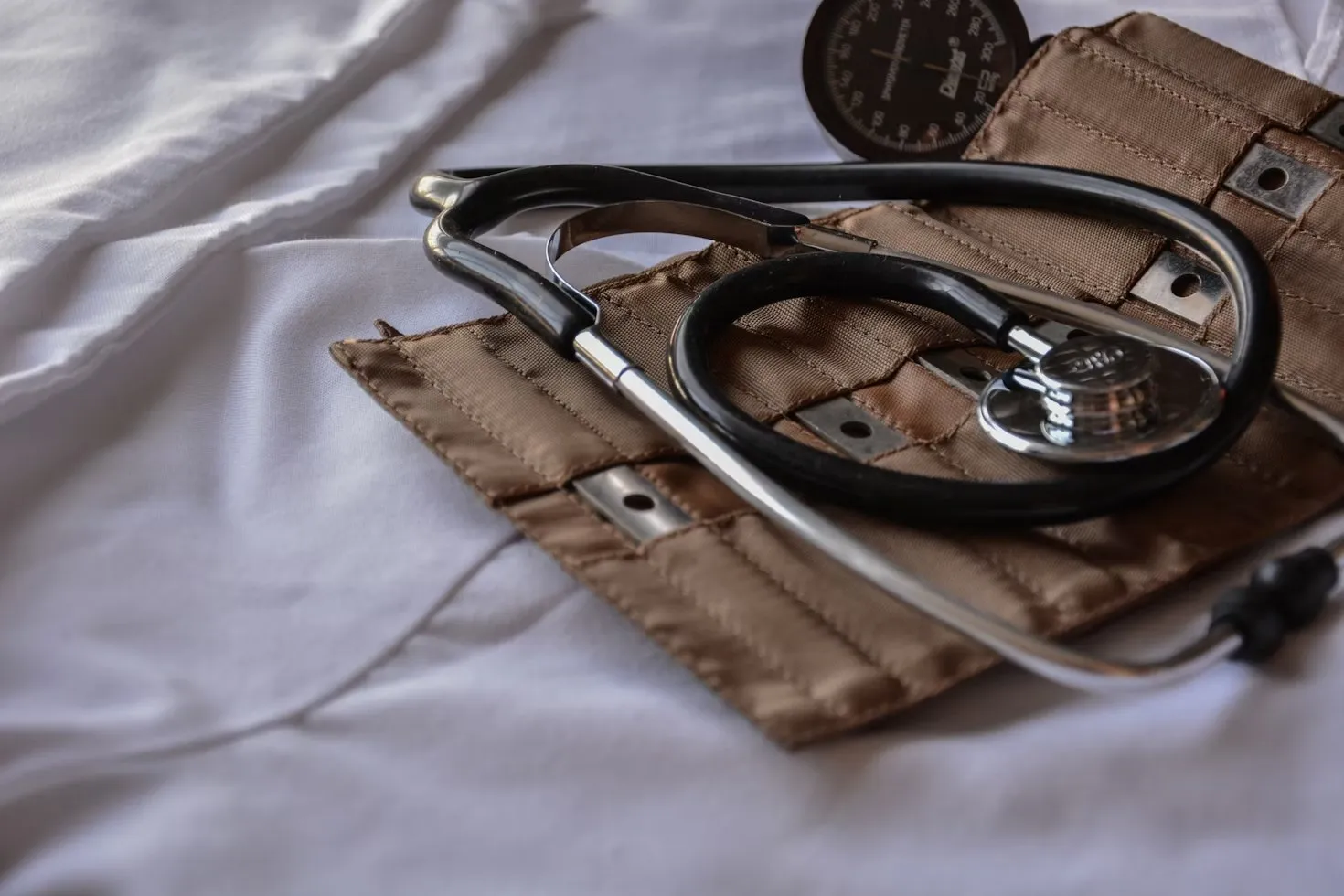 A stethoscope and a blood-pressure cuff resting on a white bed