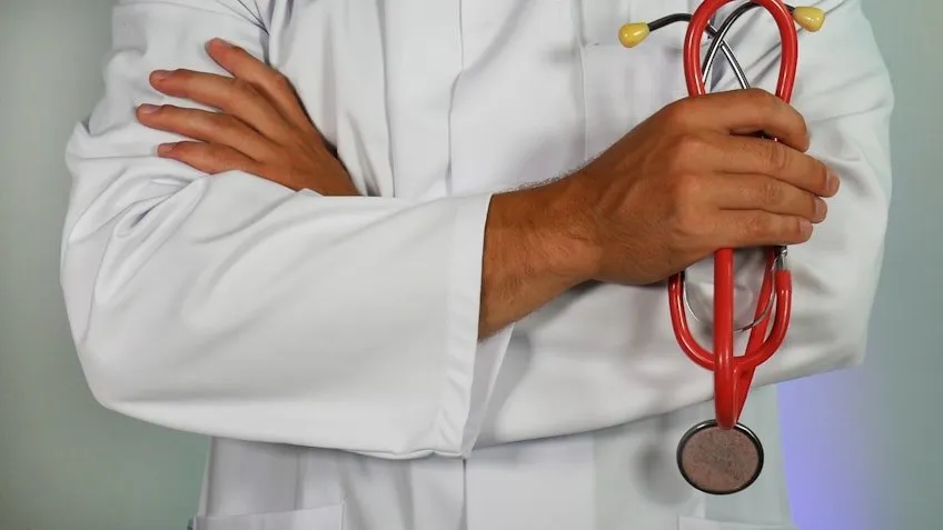 A doctor with crossed arms holding a red stethoscope