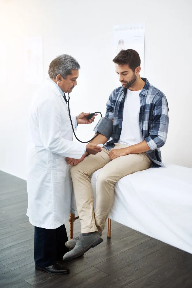 An older doctor checking a young man’s blood pressure